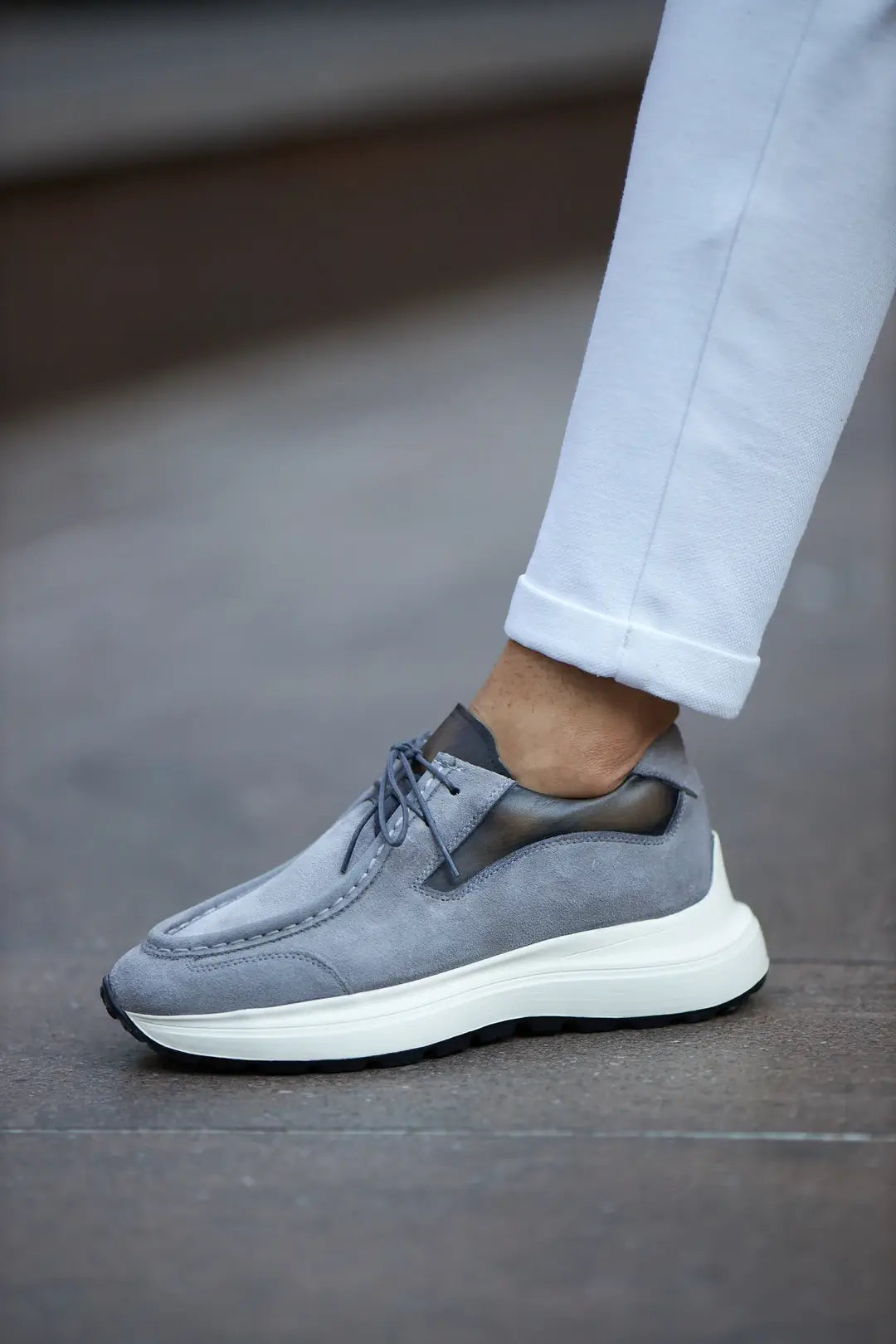 A stylish pair of gray suede smart casual shoes, designed by HolloMen, worn with white pants on a sidewalk.