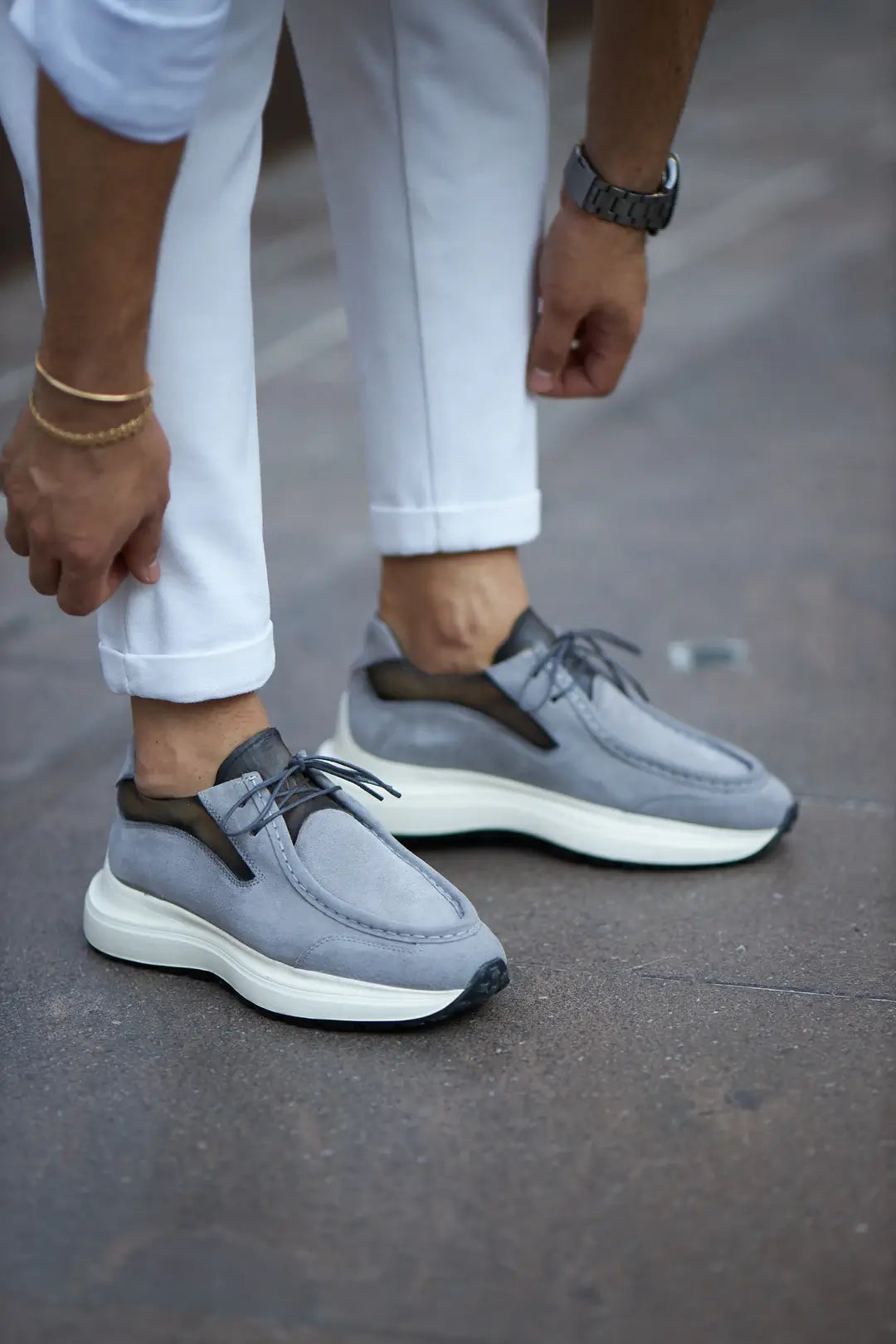 A stylish pair of gray suede smart casual shoes, designed by HolloMen, worn with white pants on a sidewalk.