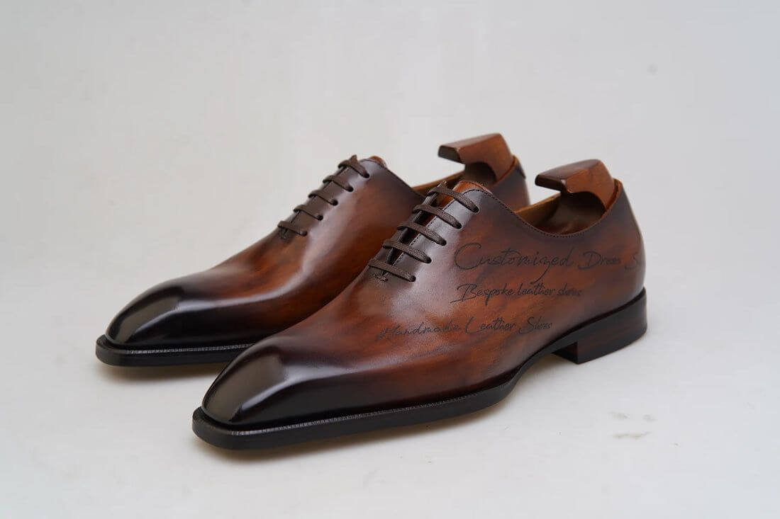 Elegant pair of handcrafted chestnut brown patina oxford shoes displayed on a wooden surface in a luxurious setting, surrounded by shoe care tools and accessories.