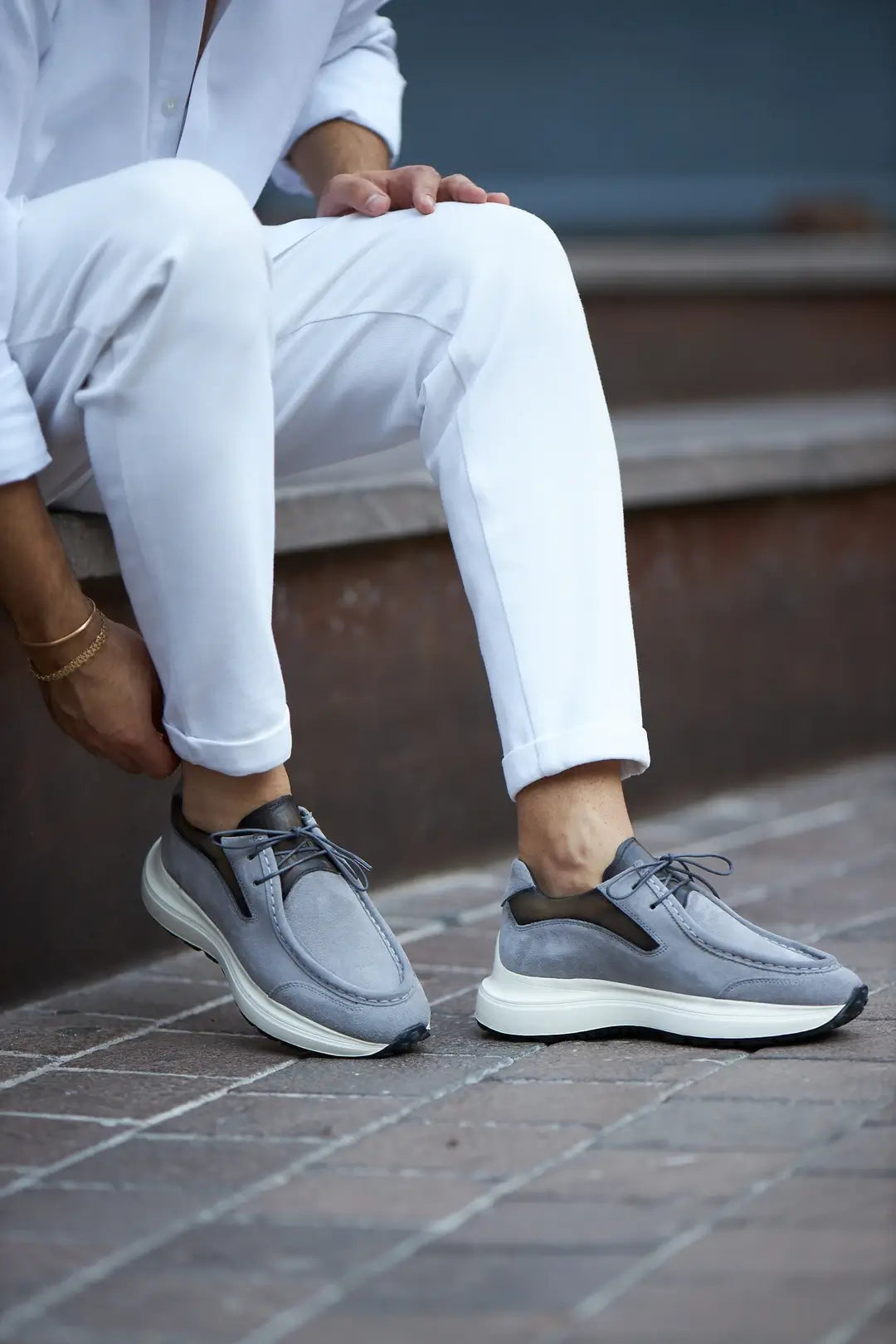 A stylish pair of gray suede smart casual shoes, designed by HolloMen, worn with white pants on a sidewalk.