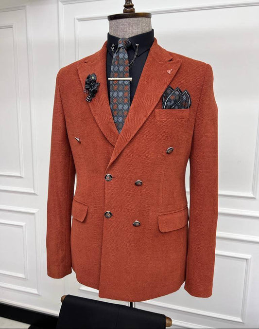 Stylish brick-red double-breasted blazer displayed on a mannequin, paired with a patterned tie, black shirt, and matching pocket square, complete with a lapel pin, set against a white paneled background.